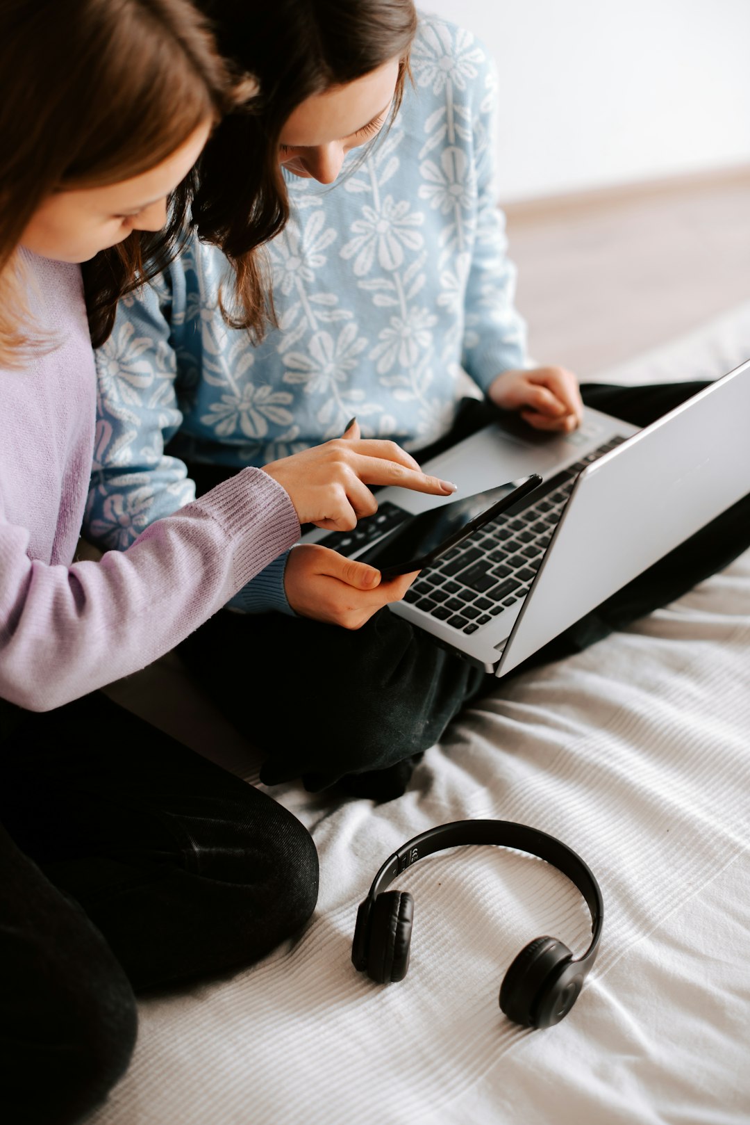 two-girls-sitting-on-a-bed-using-a-laptop-vwaw6x3mhka